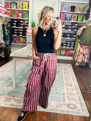 Burgundy wide-leg striped pants with side pockets and white vertical stripes, standing