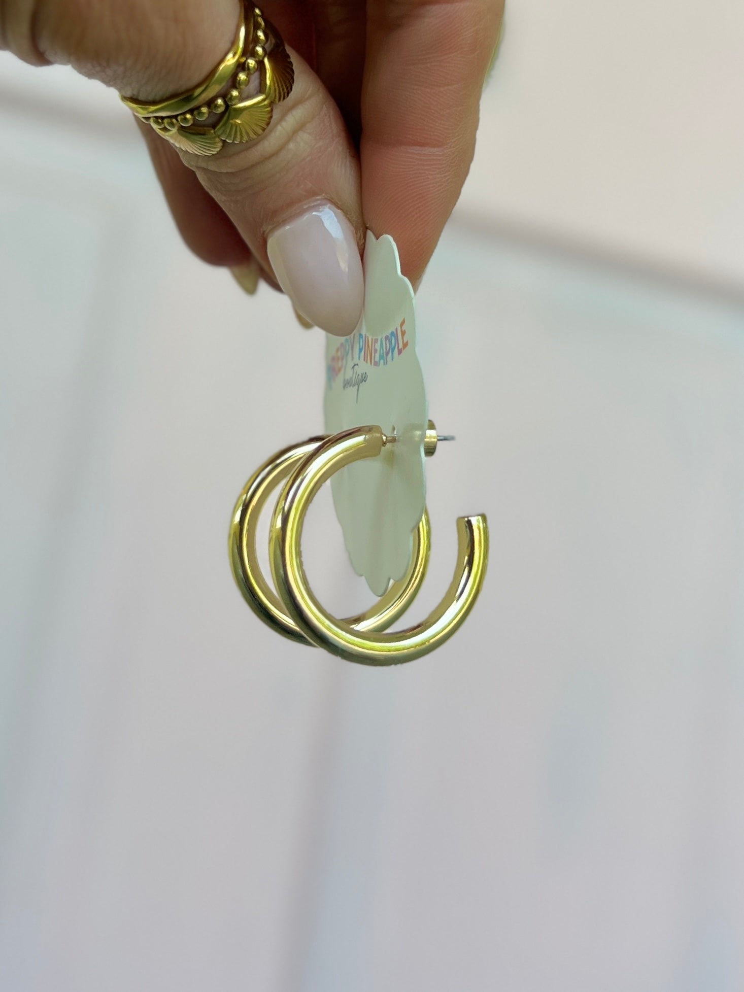 Gold metal hoop earrings with stacked rings, held by hand
