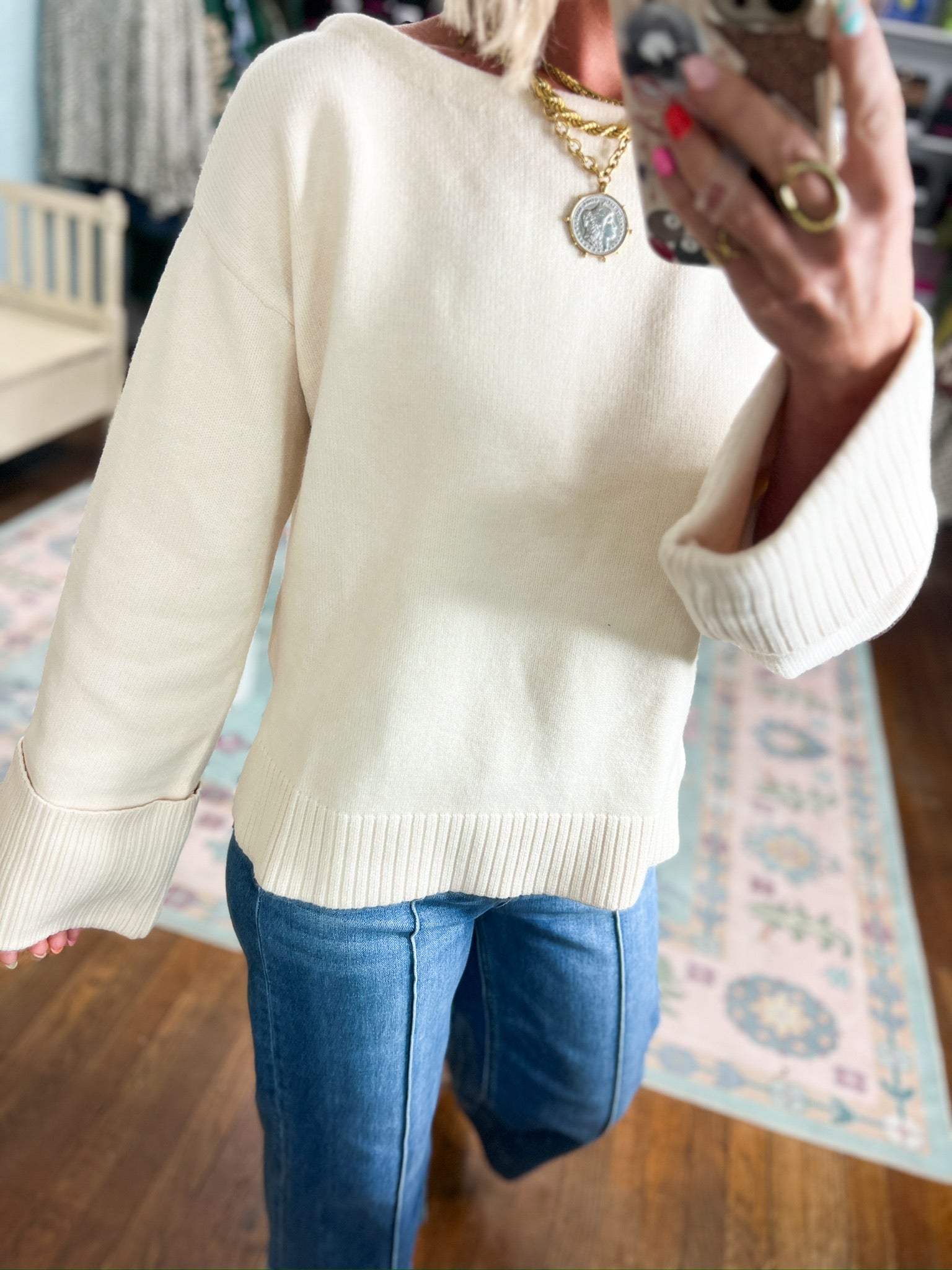 Ecru knit sweater with ribbed cuffs and hem detail, styled over blue jeans.