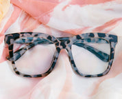 Gray tortoise eyeglasses resting on patterned fabric, rectangular clear lenses