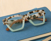 Tortoise eyeglasses angled on blue case, green-tinted lenses and brown temples