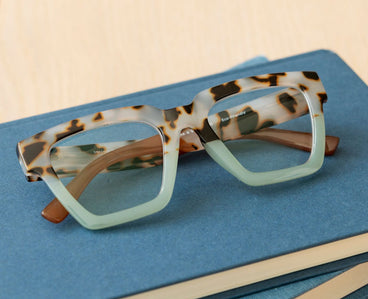 Tortoise eyeglasses angled on blue case, green-tinted lenses and brown temples