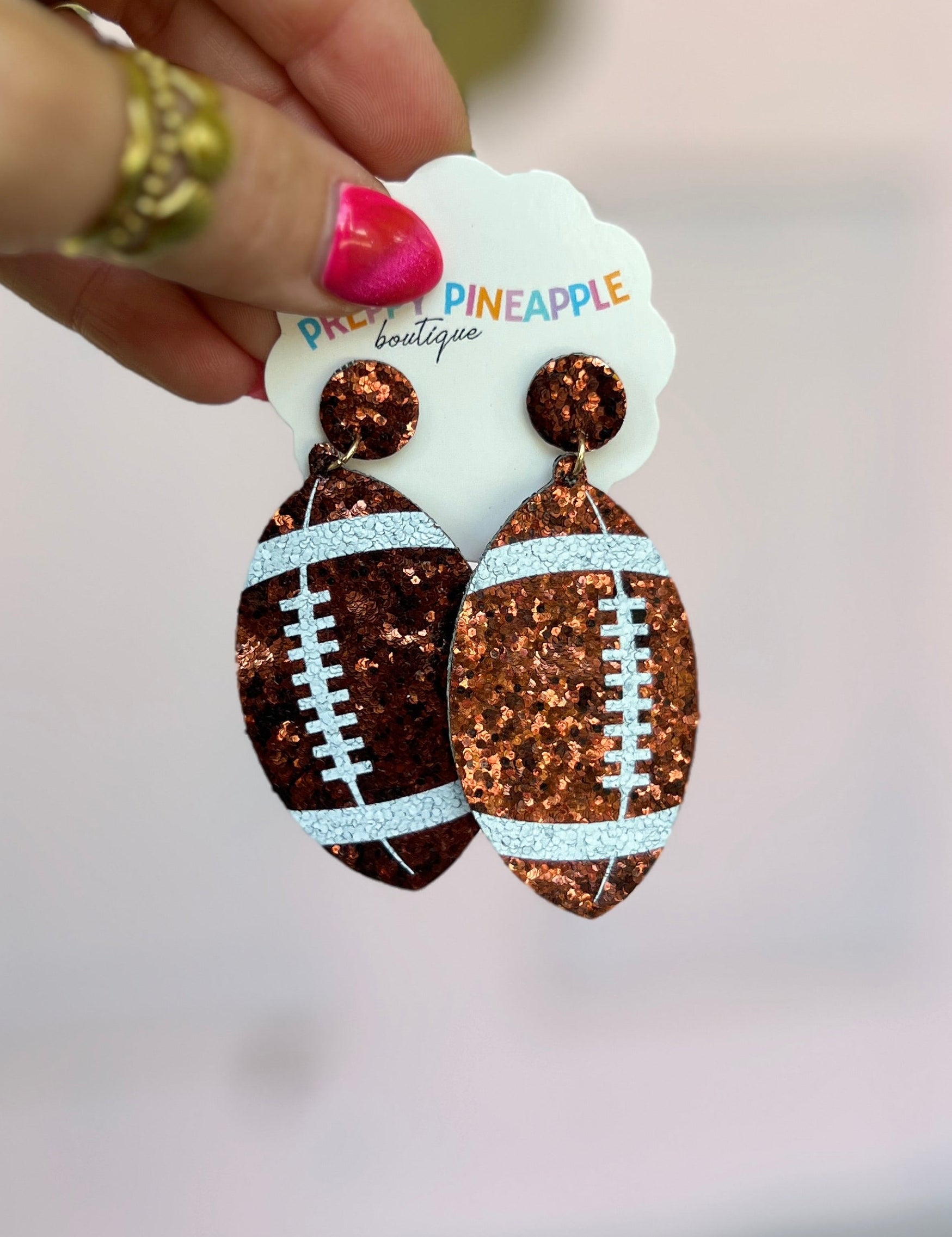 Brown glitter football drop earrings with white stitch detail and round stud tops.