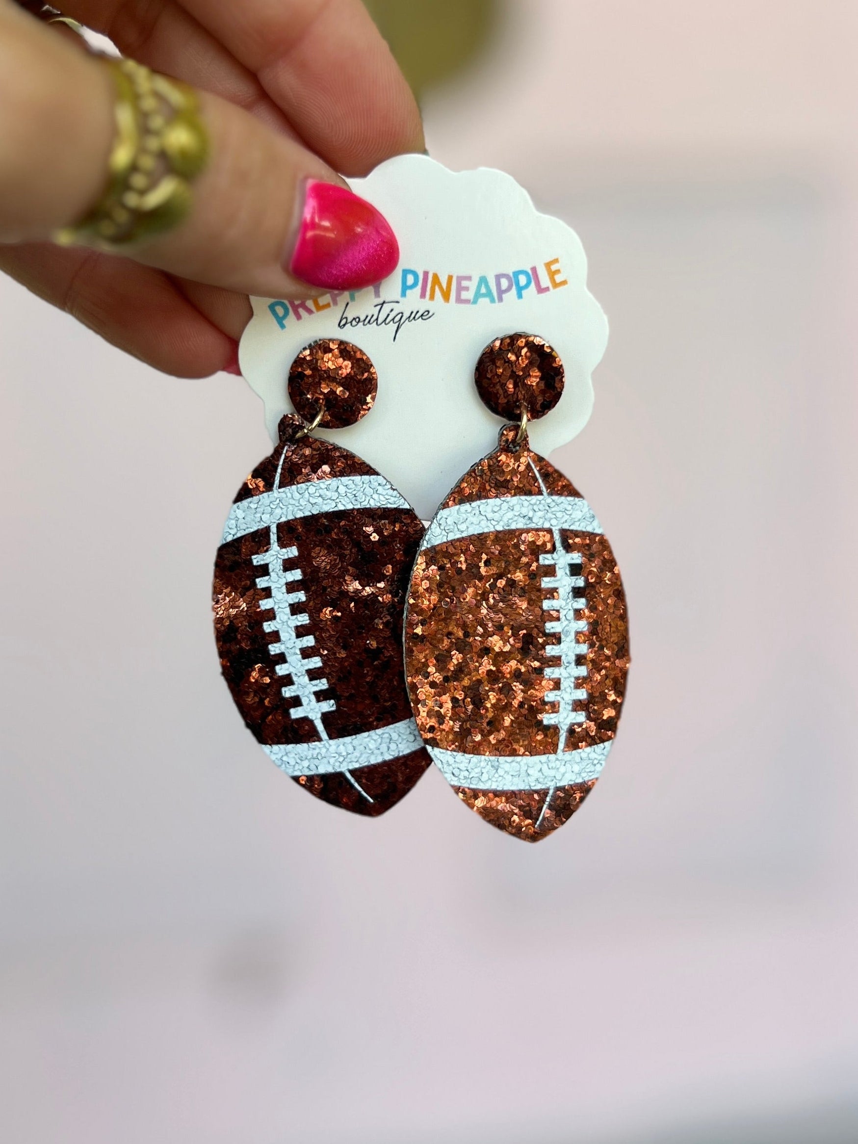 Brown glitter football drop earrings with white stitch detail and round stud tops.
