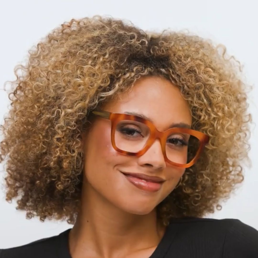 Orange tortoise-effect eyeglass frames on a model with curly hair