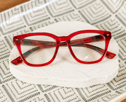Red eyeglasses with tortoise-look temples and clear lenses on white cushion