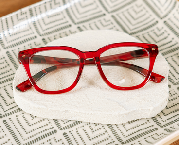 Red eyeglasses with tortoise-look temples and clear lenses on white cushion