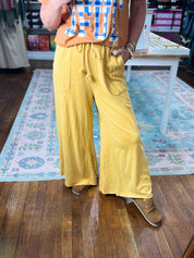 Mustard wide-leg pants with drawstring waist and side pockets, flowing drape.