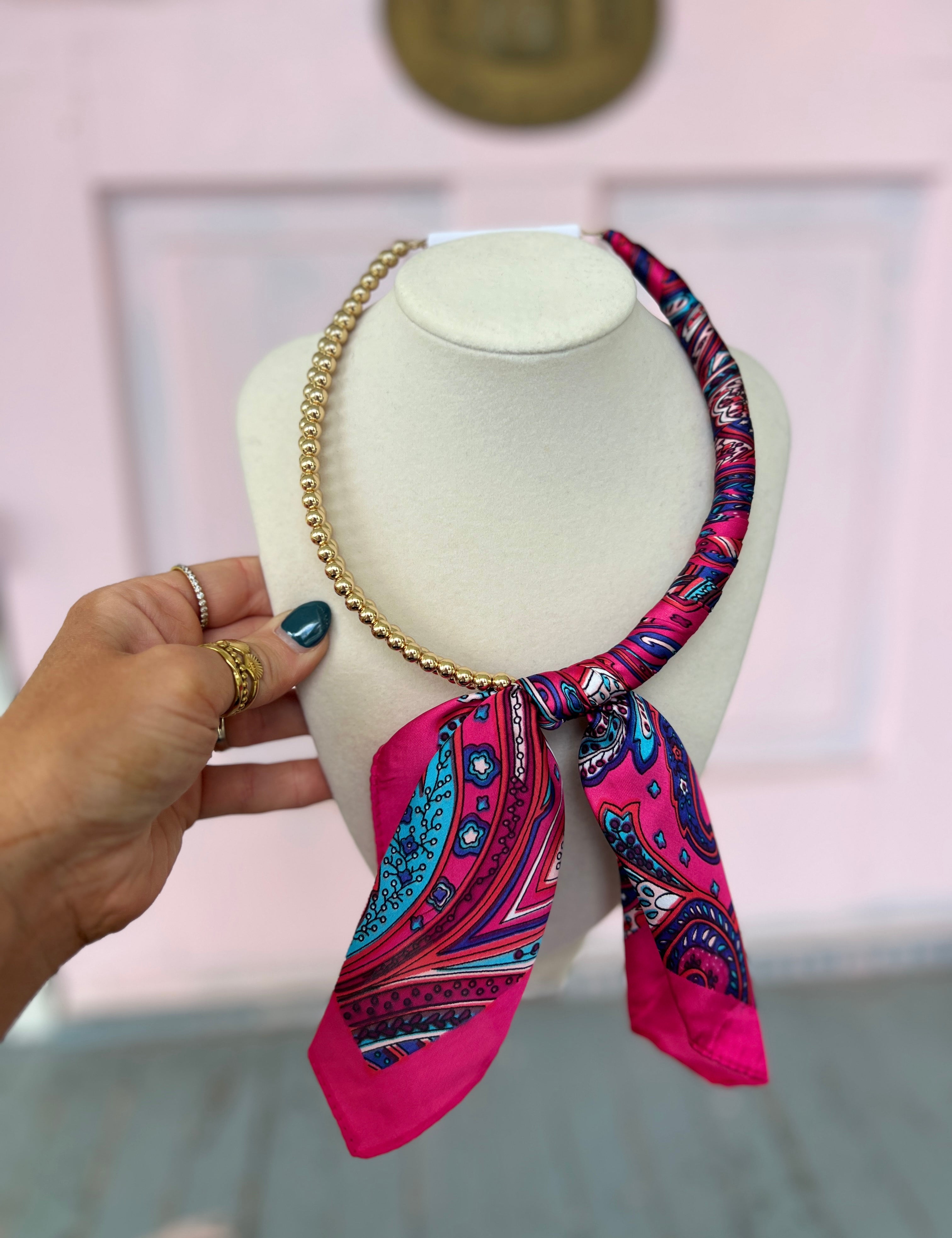 Fuchsia patterned scarf necklace with gold chain and tied ribbon scarf on mannequin