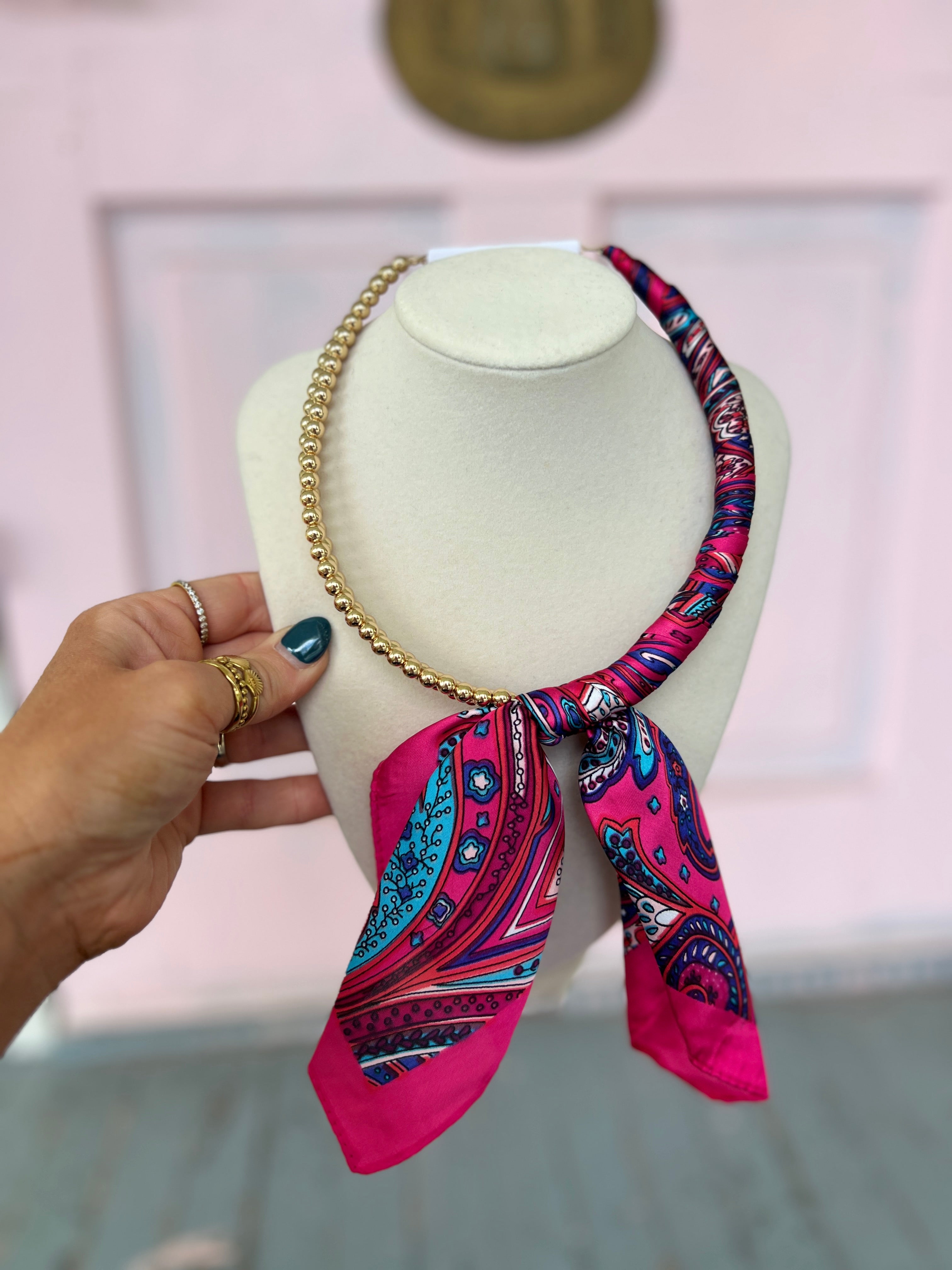 Fuchsia patterned scarf necklace with gold chain and tied ribbon scarf on mannequin