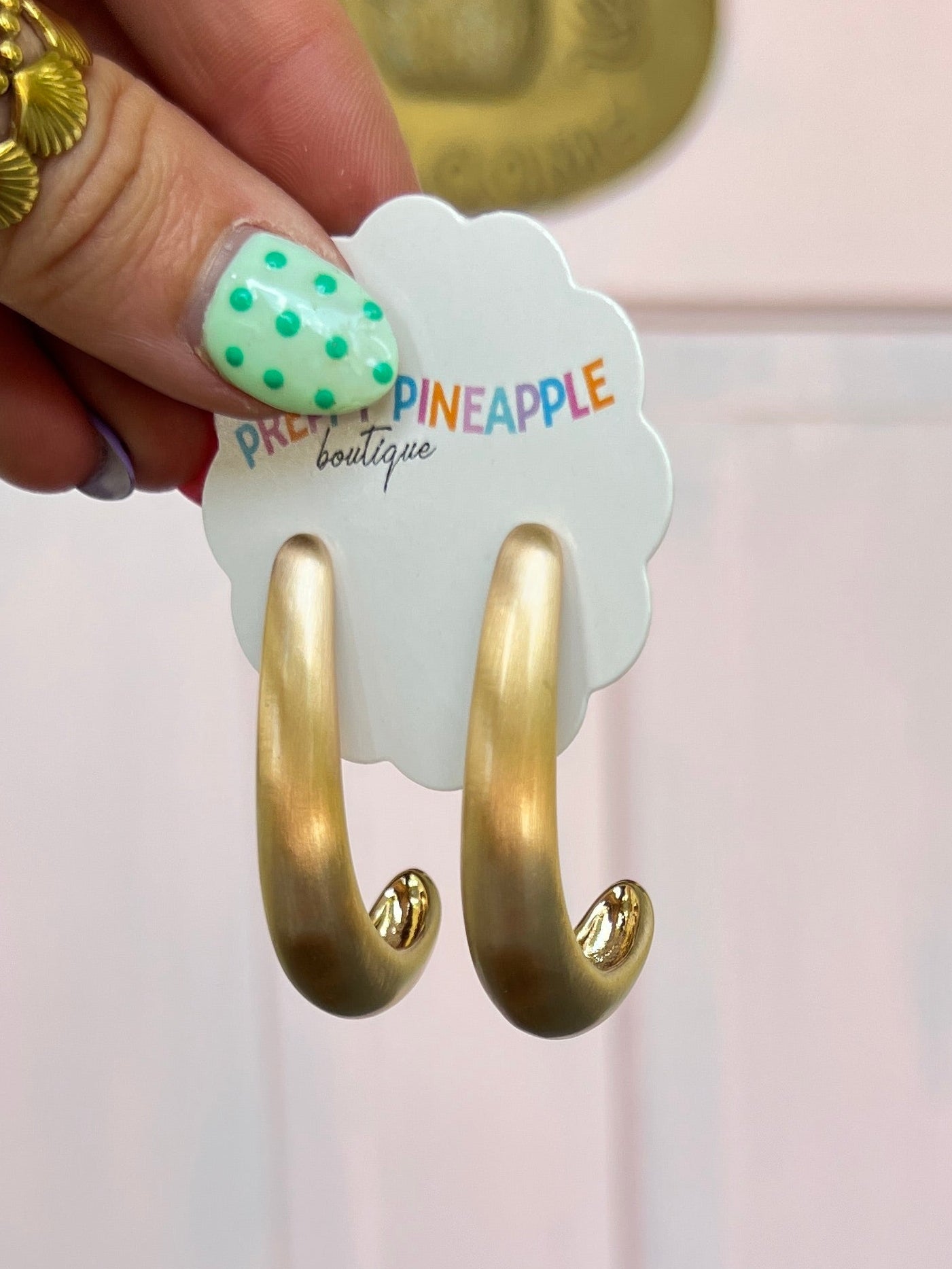Matte gold curved hoop earrings with hook backs, close-up on hand