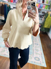 Close-up of champagne faux suede V-neck top with scalloped hem and long puff sleeves.