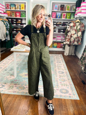 Olive patterned twill overalls with bib front and wide legs, worn with black sneakers