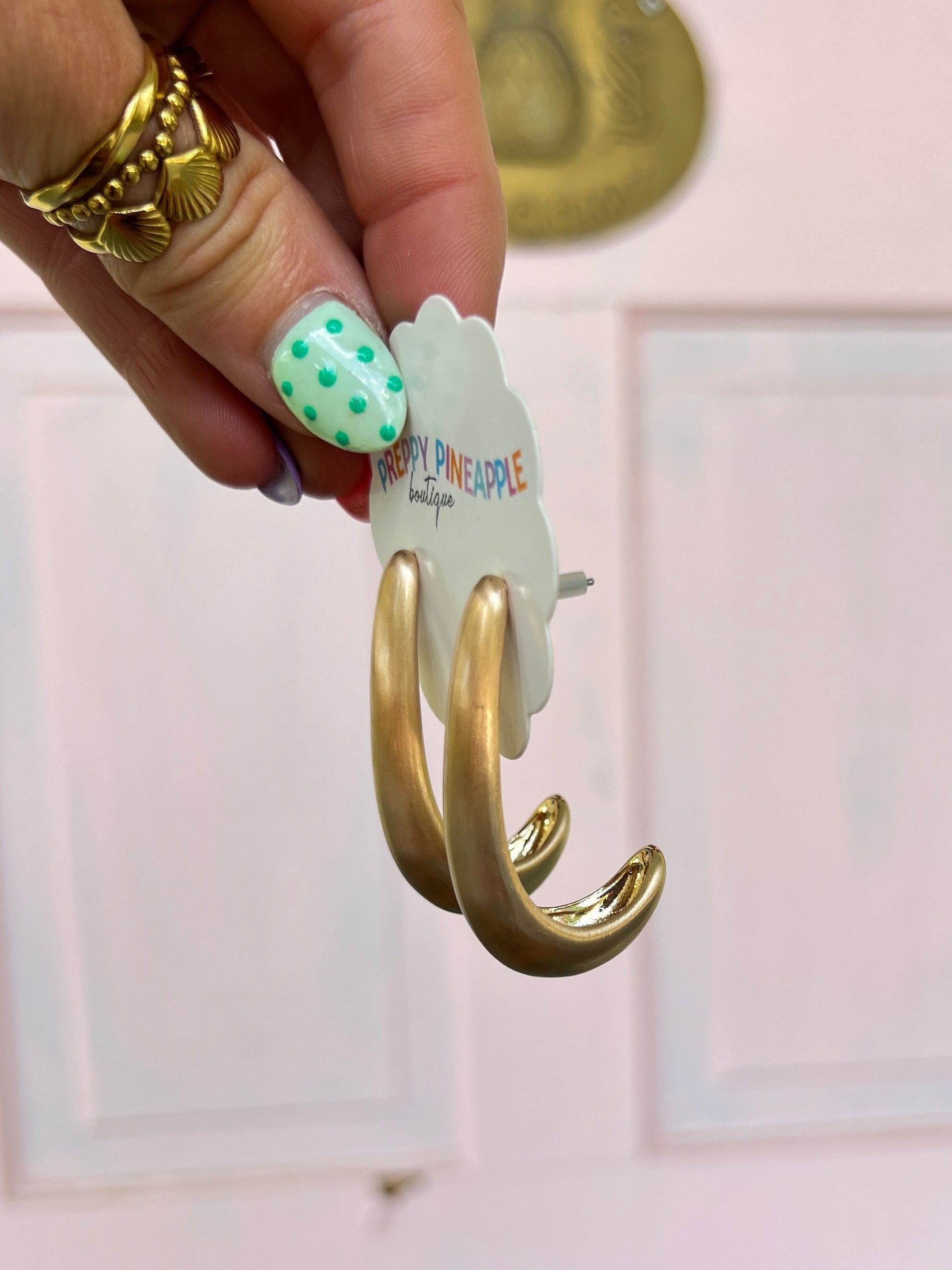 Matte gold curved hook hoop earrings on hand, polished metal finish