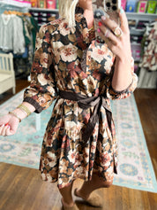 Long-sleeve floral dress with ruched tie waist detail, black background close-up