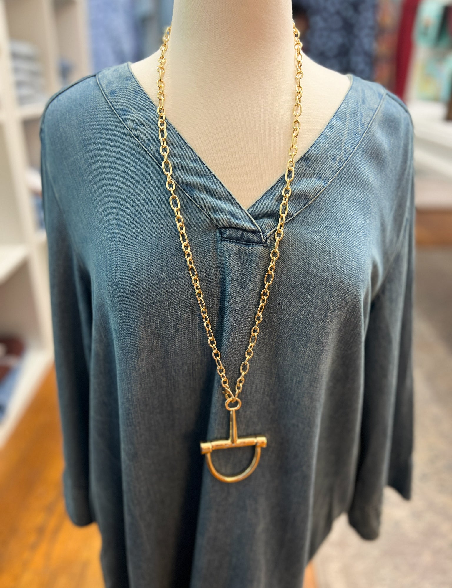Gold horsebit pendant necklace with linked chain, worn on a crew-neck top.