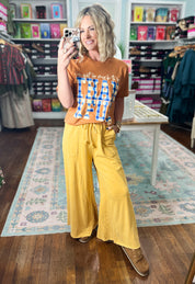 Mustard wide-leg pants with gathered drawstring waist and side pockets, full length.