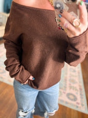 Dark brown knit off-shoulder sweater close-up, long sleeves and ribbed cuffs