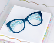 Navy eyeglasses with blue patterned temples shown at an angle on a display card