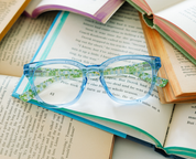 Light blue eyeglasses with green patterned temples on open book pages