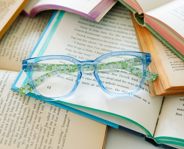 Light blue eyeglasses with green patterned temples on open book pages