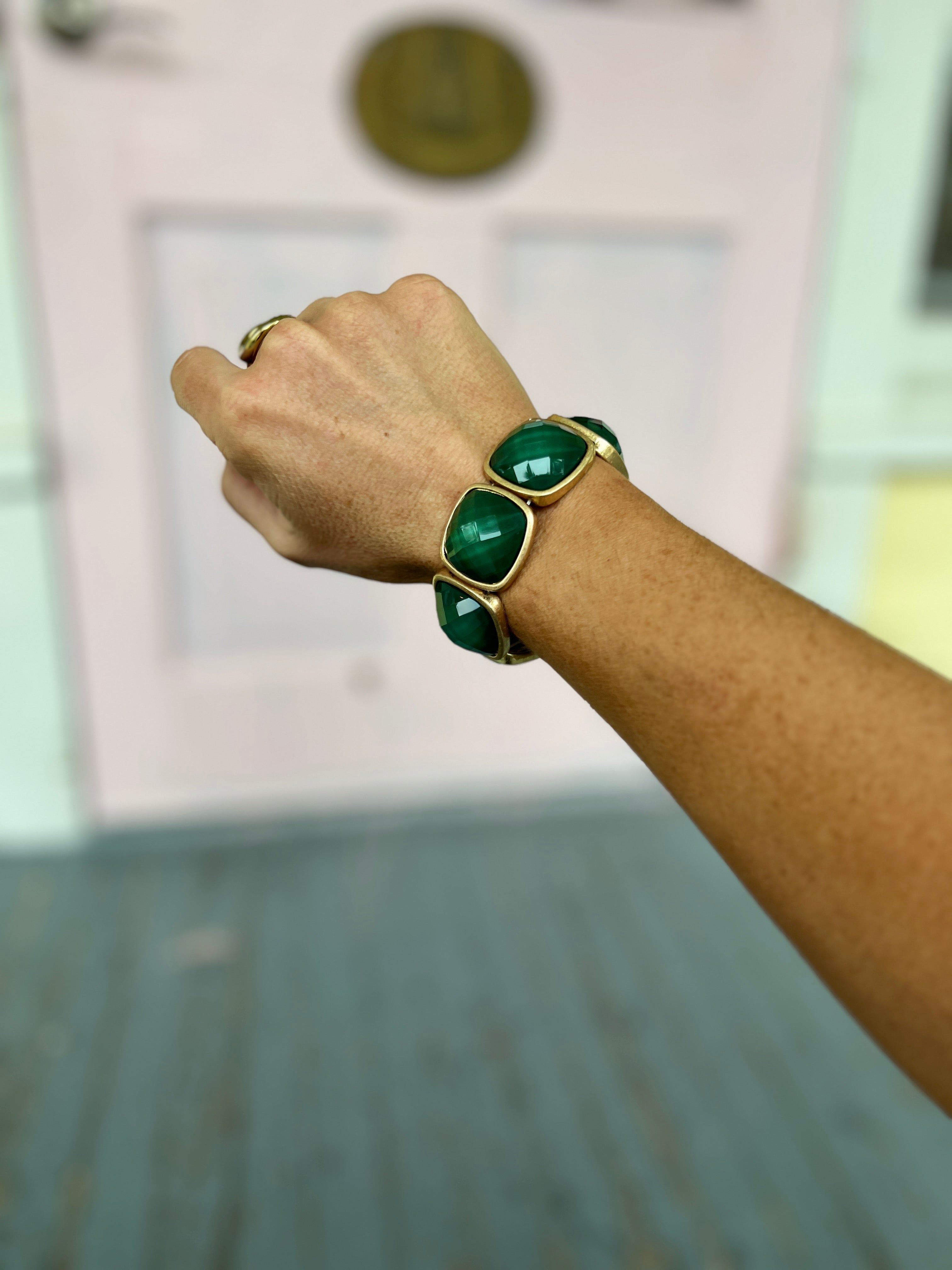Gold-tone statement bracelet with dark green square stone links on wrist