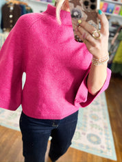 Fuchsia mock neck knit sweater with ribbed neckline and cuffs, side view over jeans