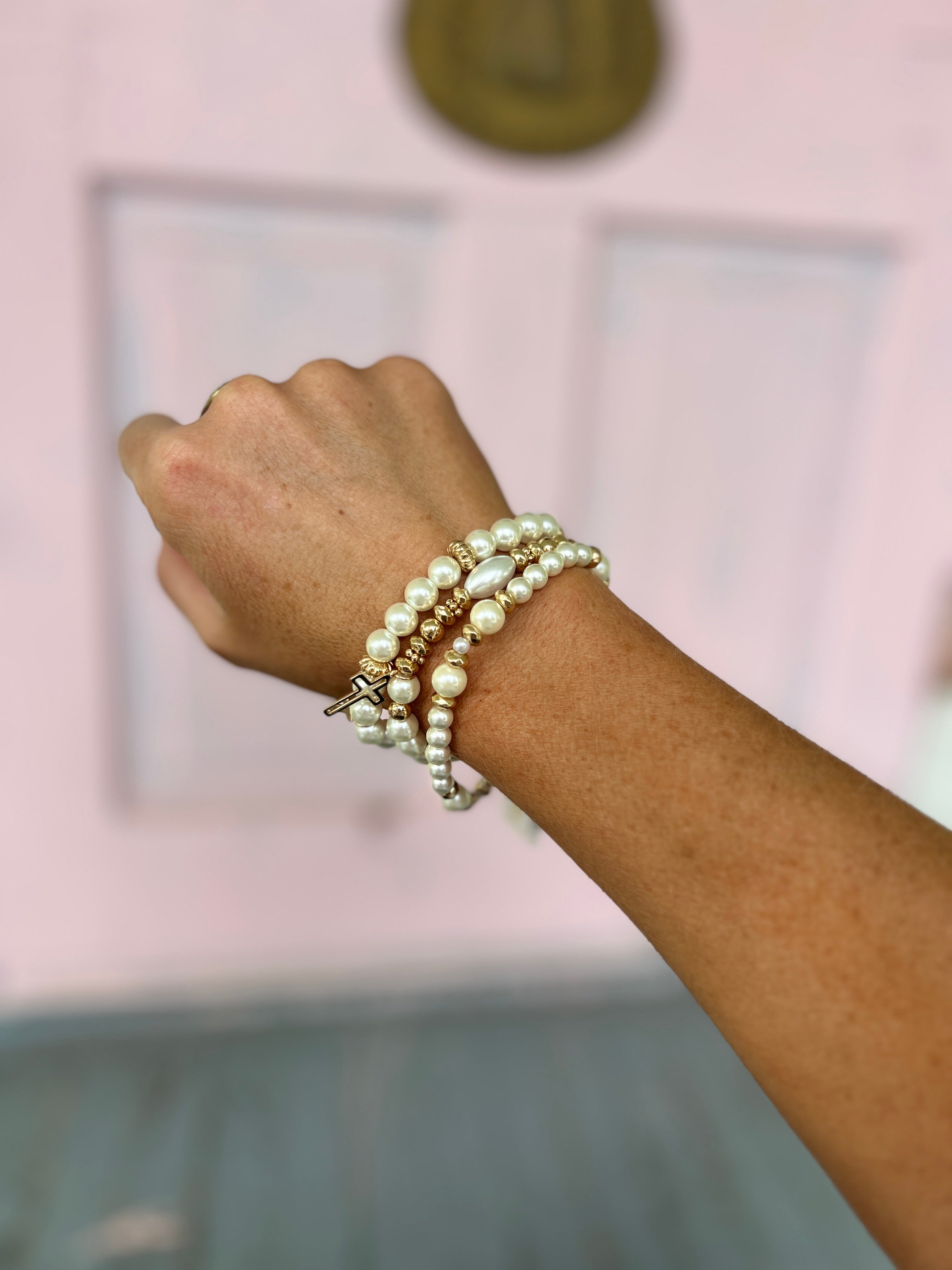 Cream pearl beaded bracelet set with gold cross charms, layered on wrist