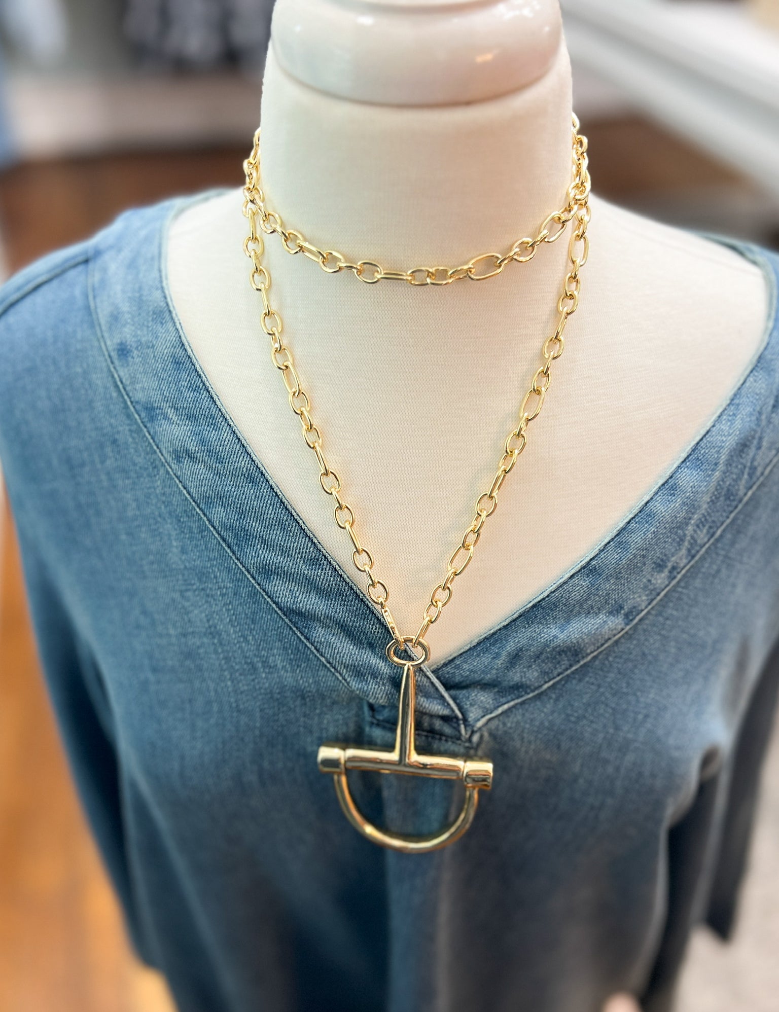 Gold horsebit pendant necklace with oval bar charm on linked chain, close-up.
