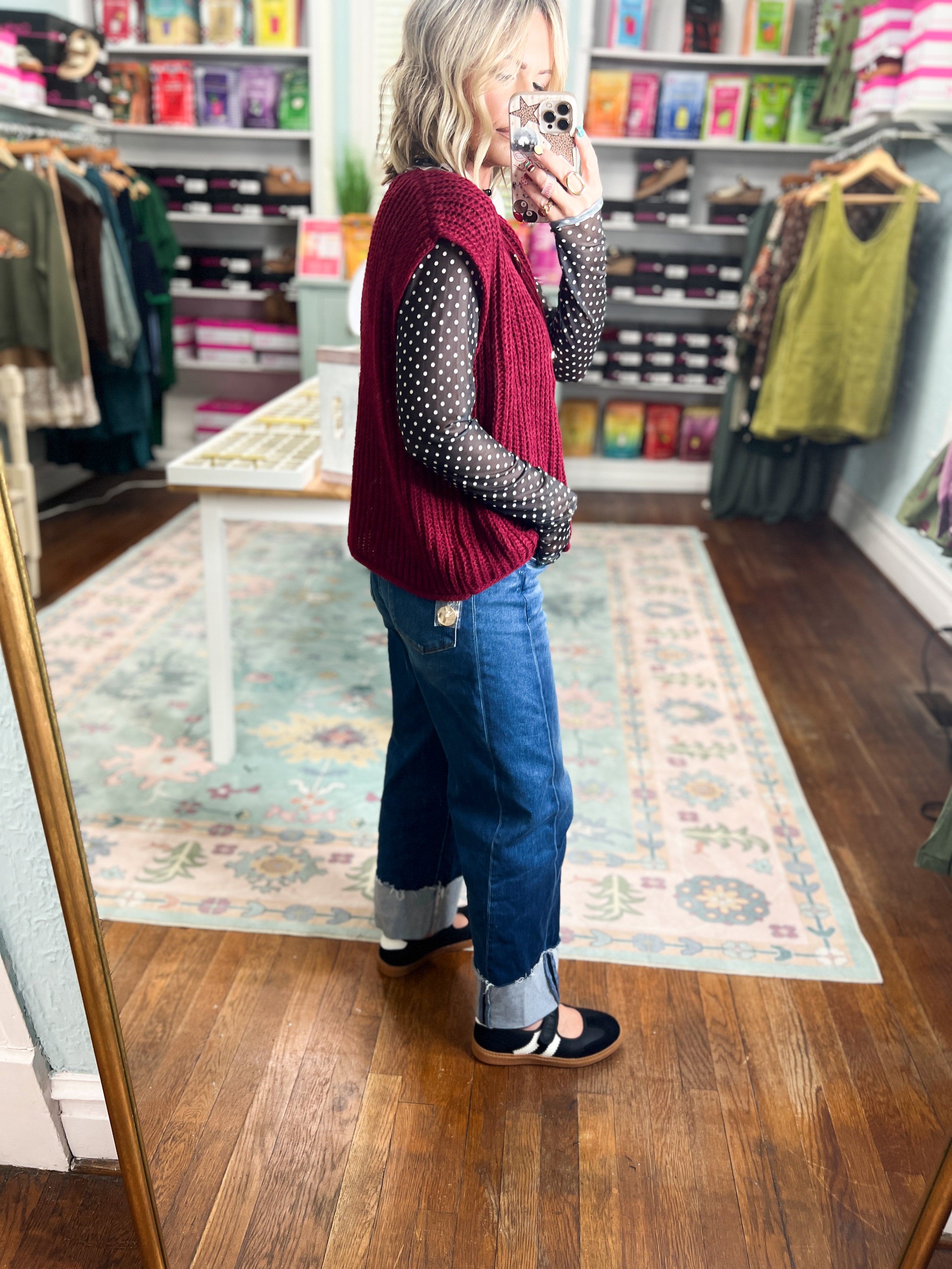 Burgundy sleeveless knit button sweater with ribbed texture, worn over dotted long sleeves.