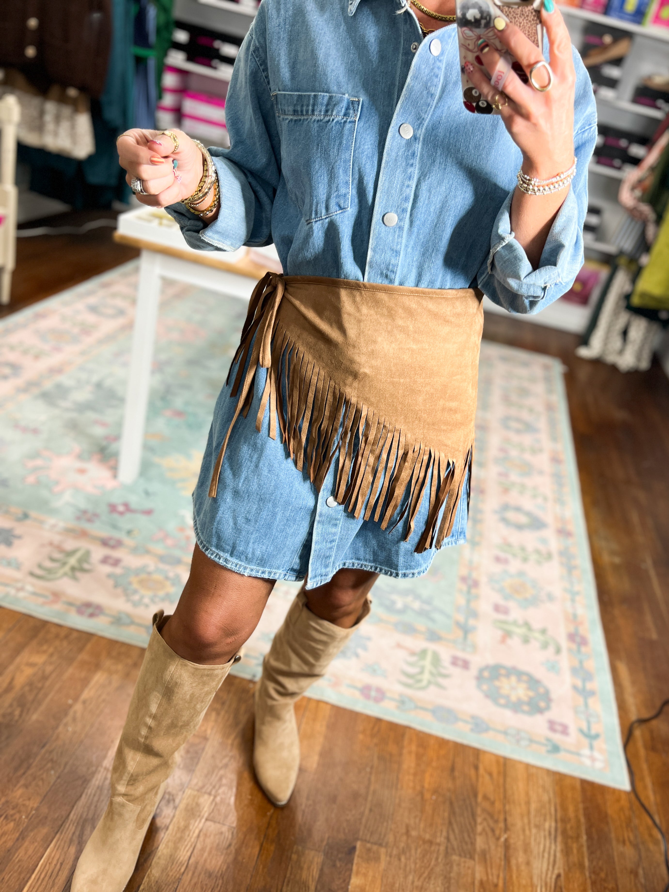 Tan suede triangle scarf with fringe trim, worn at the waist over denim.