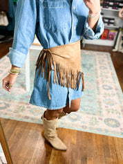Tan suede triangle scarf with long fringe trim, draped at the waist over denim.