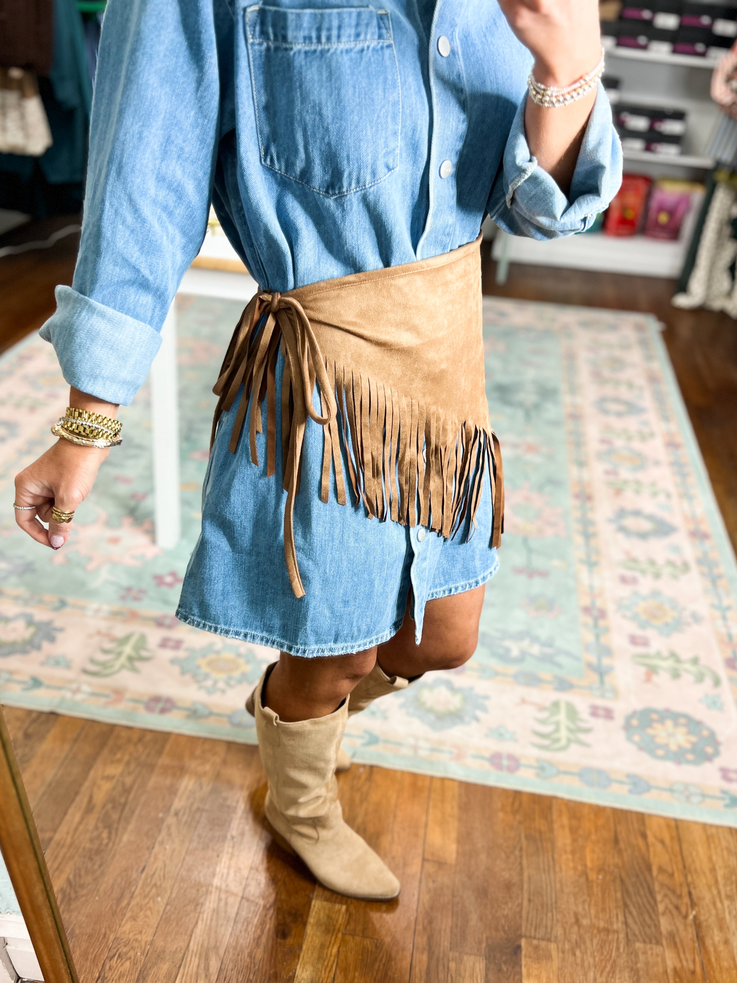 Tan suede triangle scarf with long fringe trim, draped at the waist over denim.